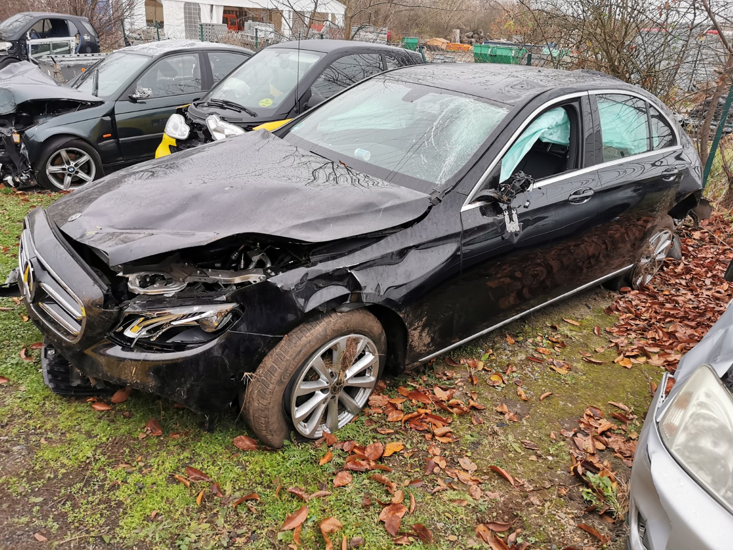 Schwarz beschädigtes Auto mit geöffneter Motorhaube; Herbstlaub auf Boden verstreut.