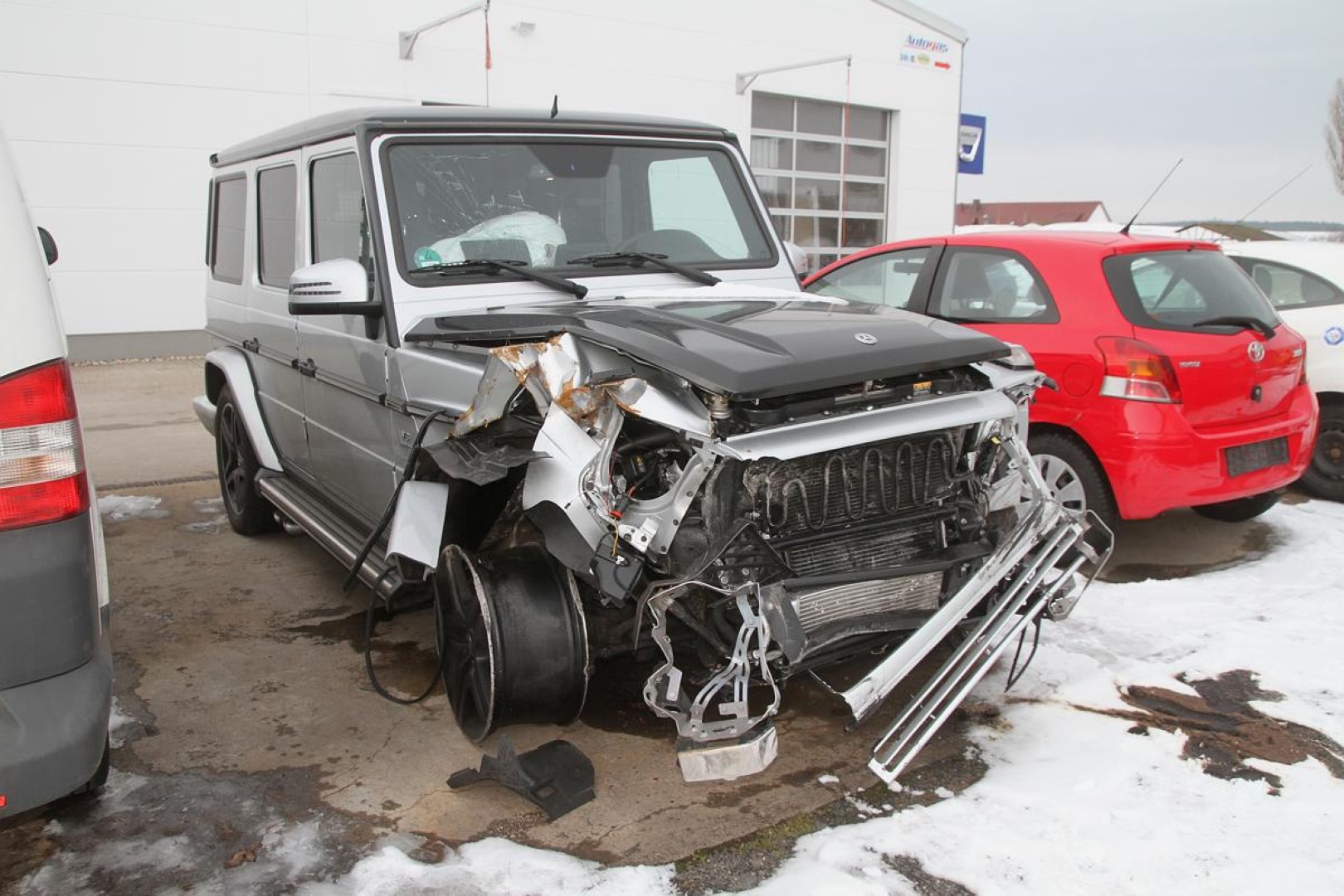 Silberner SUV mit stark beschädigter Front, umgeben von Schnee und anderen geparkten Autos.