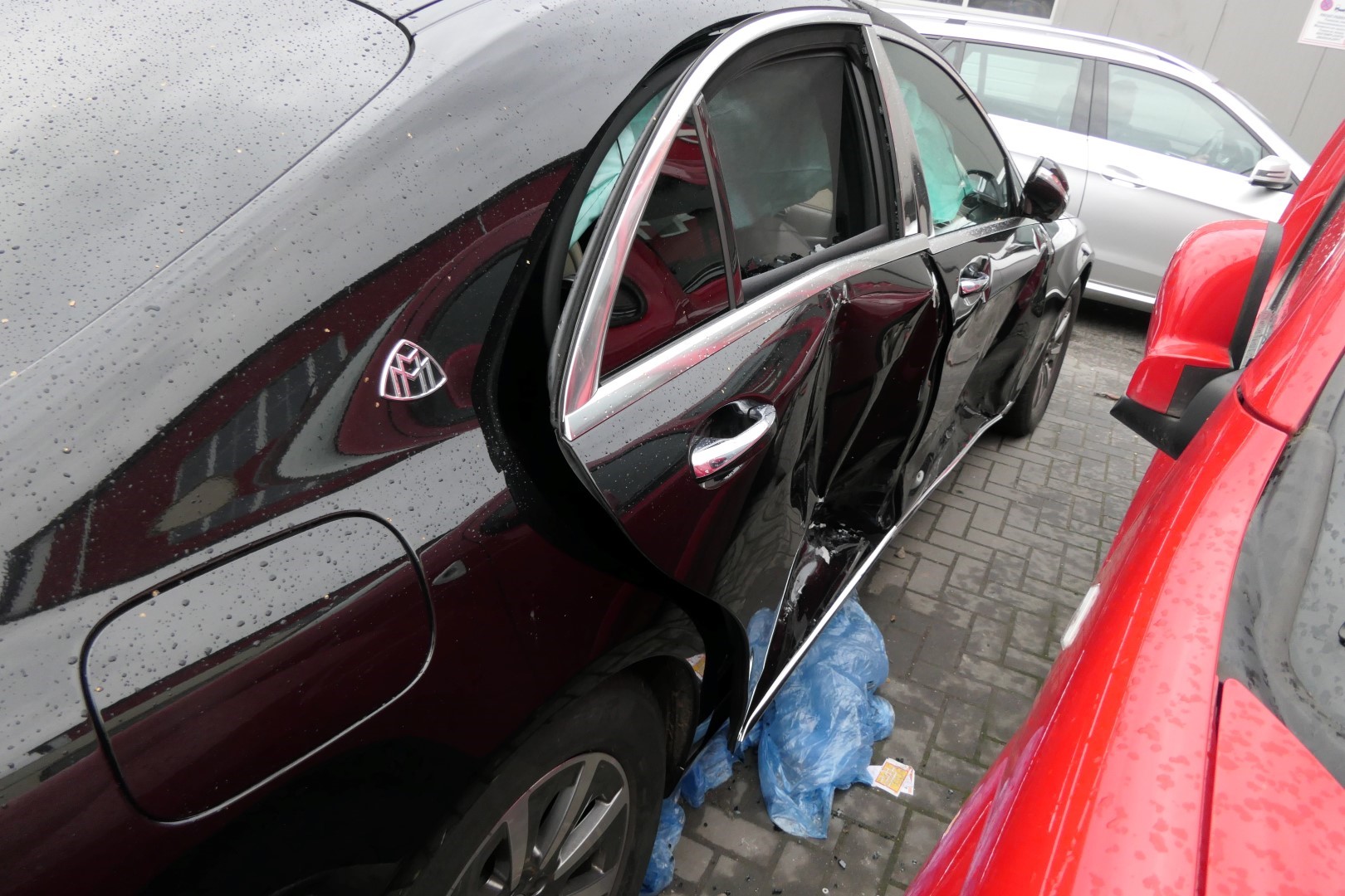 Beschädigtes schwarzes Auto, Beifahrerseite eingedellt, verregnete Umgebung.