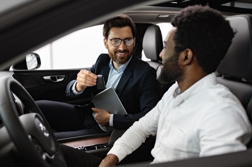 Autohändler, der dem Käufer im Inneren des Fahrzeugs hilft, im Autohaus