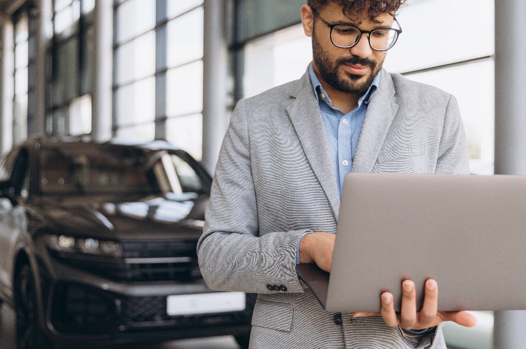 Autoverkäufer arbeitet am Laptop im Ausstellungsraum eines Autohauses