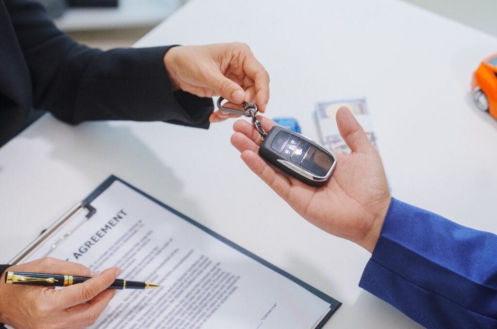 Ein asiatischer Verkäufer mittleren Alters in einem formellen Anzug hilft einer Käuferin an einem Schreibtisch. Sie schließen einen Leasingvertrag für ein Fahrzeug ab, prüfen die Finanztabellen und unterschreiben den Vertrag.