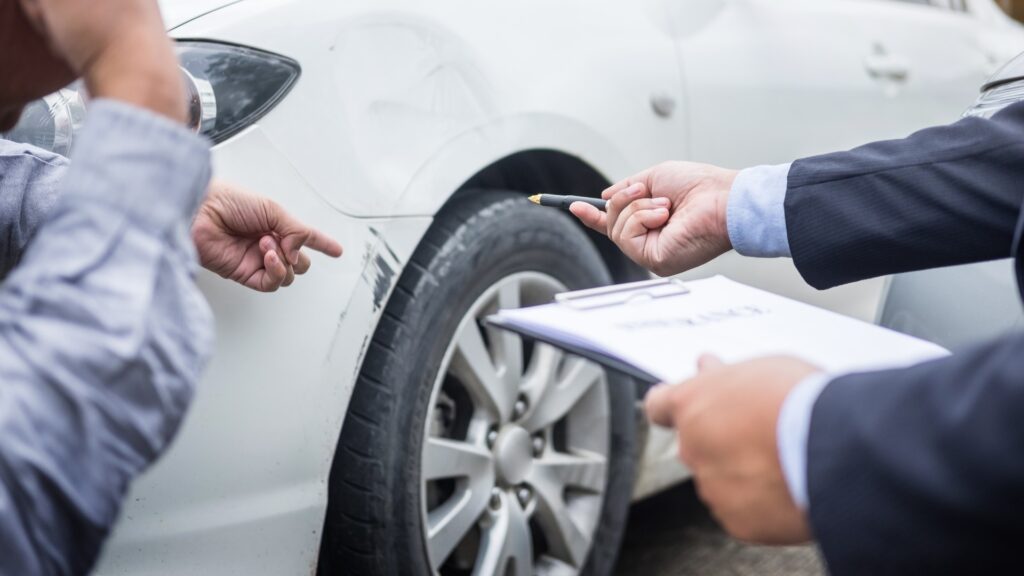 Ein Versicherungsagent, der auf einem Klemmbrett notiert, während er nach einem Unfall ein Auto begutachtet